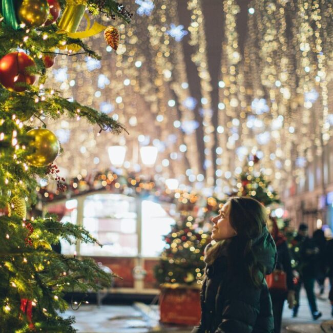 Christmas scene with a woman admiring festive decorations at a market.