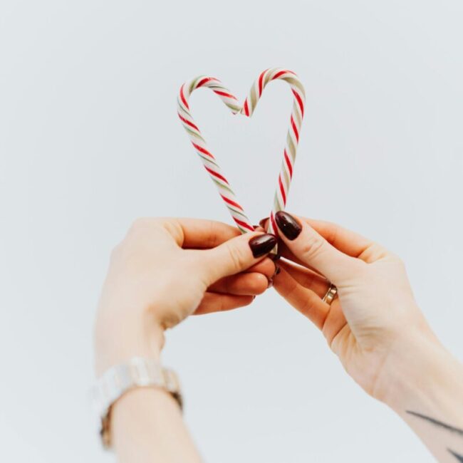 Close-up of hands holding candy canes in a heart shape, symbolizing love and holiday cheer.