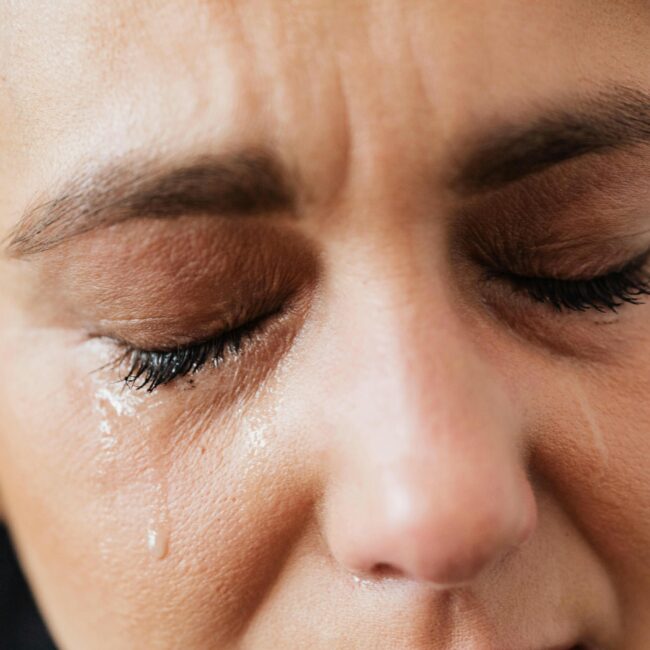 Emotional close-up of a woman's face with closed eyes and tears expressing distress.