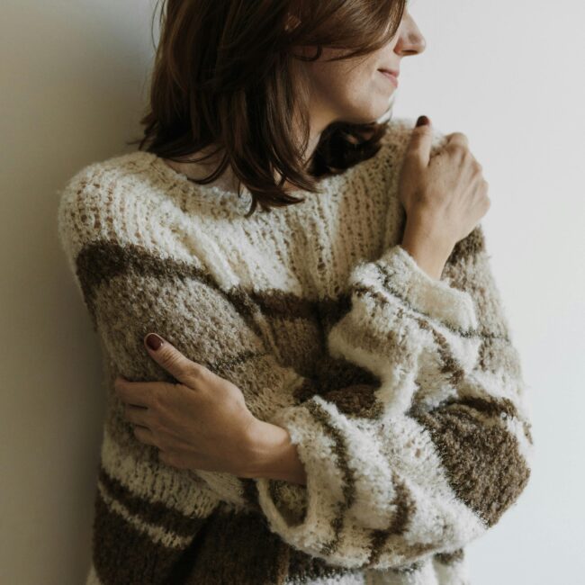 Woman in a knit sweater hugging herself with a serene expression, indoors.